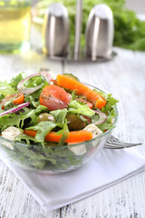 Greek salad in glass dish on napkin and color wooden background