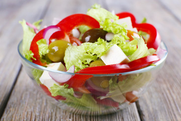 Greek salad in glass dish on wooden table background