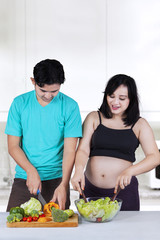 Expectant woman with husband preparing salad