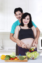 Pregnant couple cooking salad in kitchen