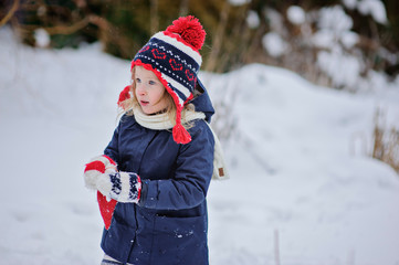 Fototapeta na wymiar child girl in knitted hat on the walk in winter snowy garden