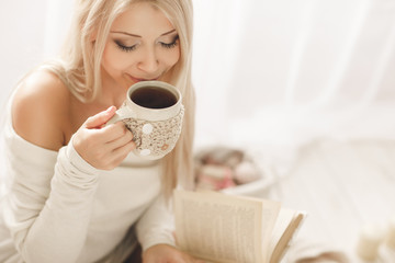 Young woman reading a book with a Cup of coffee in his hands.