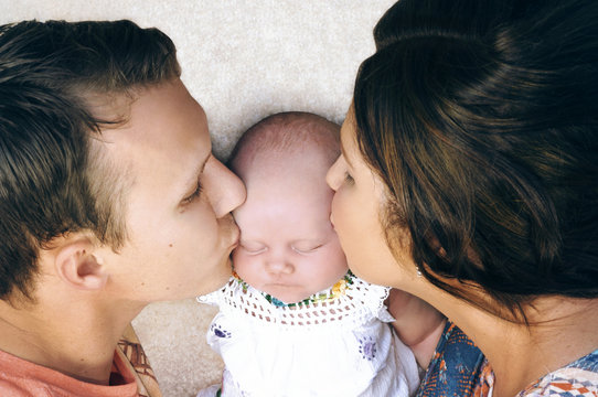 Young Couple Kissing Their Newborn Baby.