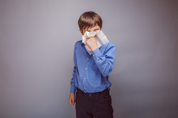 teenager boy sick sneezing into a handkerchief on gray backgro