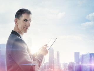 Businessman with digital tablet and blurred city on horizon