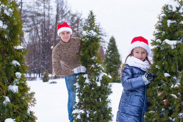 Happy father and kid in Santa hats with christmas tree outdoor