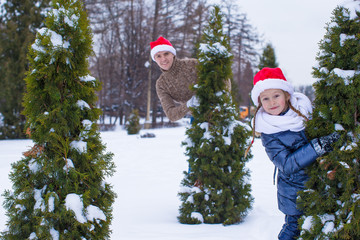 Happy father and kid in Santa hats with christmas tree outdoor