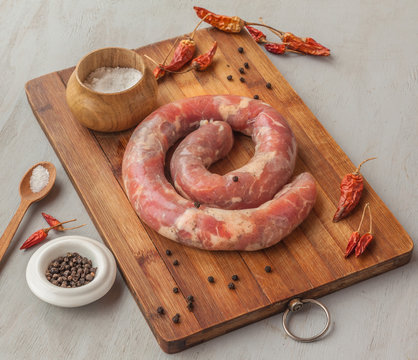 Ring of raw sausage on a cutting board with pepper