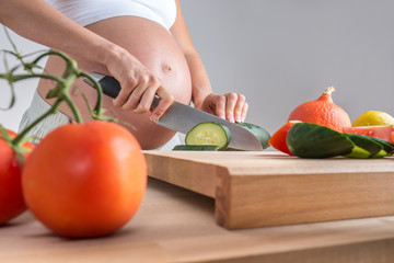 Pregnant woman standing at a kitchen counter with a wooden board - Powered by Adobe