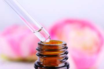 Dropper bottle of perfume with flowers on light background