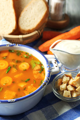 Carrot soup, cream and spoon, on  color wooden background