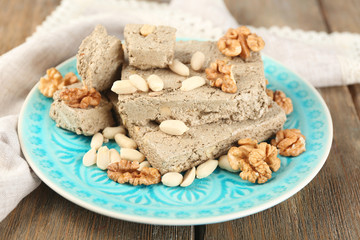 Sunflower halva with nuts on plate, on wooden background