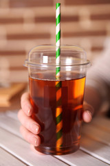 Female hand at wooden table with fast food closed cup of apple