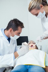Fototapeta na wymiar Male dentist with assistant examining girls teeth