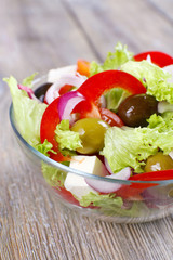 Greek salad in glass dish on wooden table background