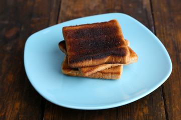 Burnt toast bread on turquoise plate, on wooden table