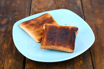 Burnt toast bread on turquoise plate, on wooden table
