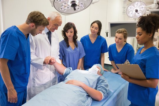 Medical students and professor checking pulse of student