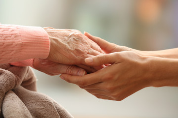 Old and young holding hands on light background, closeup