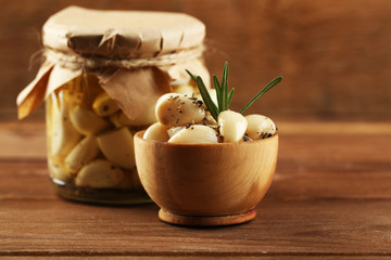 Canned garlic in glass jar and bowl on wooden background