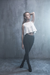 Fashionable young girl standing on a gray background textured wa