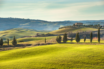Artistic Tuscan landscape with cypresses, wavy fields and house