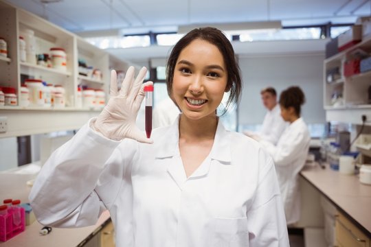Pretty science student smiling and showing vial