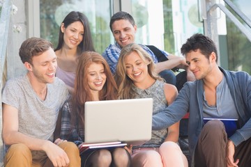 Happy students looking at laptop outside