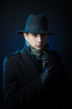 Young man in black trench coat standing in the darkness