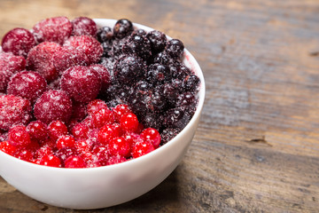 frozen berries in plate on wooden background