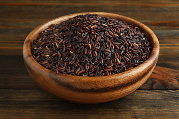 Black rice in a wooden bowl on wood closeup