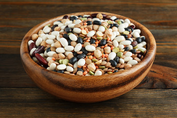Mix of beans in a wooden bowl on wood closeup