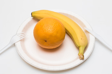 Juicy orange and banana on white plate isolated on white