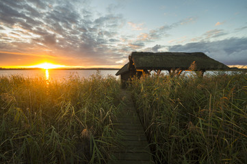 Zachód słońca nad jeziorem,do jeziora prowadzi drewniany pomost 