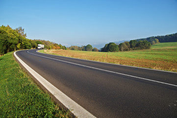 Asphalt road in the countryside, white truck coming around