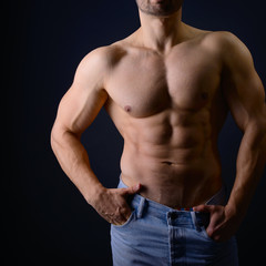 Strong athletic man with perfect body posing in studio on black