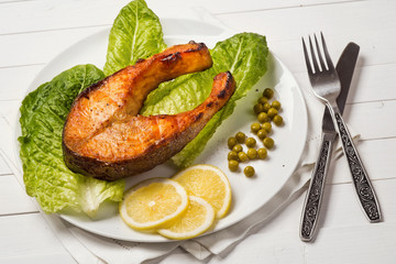 Fried trout with a piece of lettuce, lemon and green peas