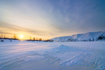 Fototapeta na wymiar Winter landscape with frozen river and hills at sunset