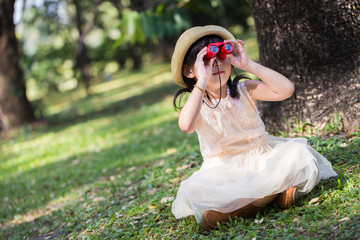 Little asian girl looking trough a binoculars in park