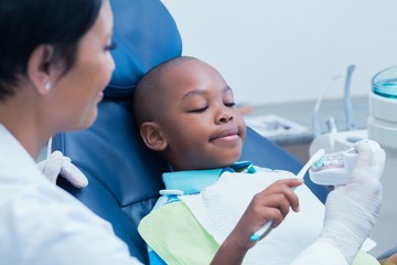 Female dentist teaching boy how to brush teeth