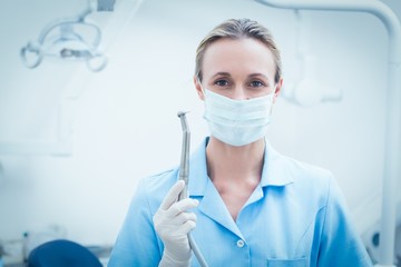 Female dentist in surgical mask holding dental tool