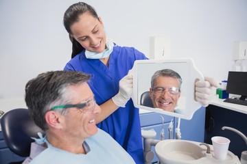 Fototapeta premium Smiling dentist showing teeth of her patient with a mirror