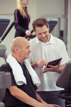 trainer erklärt einem senior im fitness-studio den trainingsplan