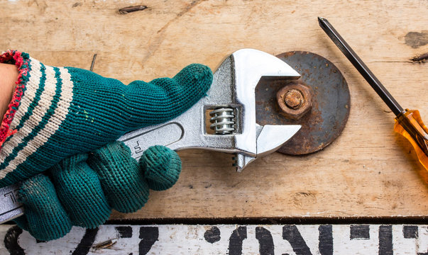 hand holds wrench and tighten the nut on the wooden floor.