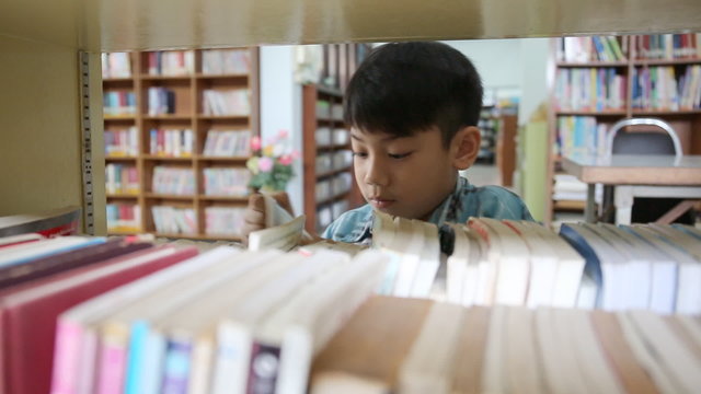 Little Asian student reading book in library .