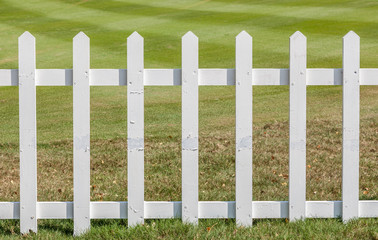 Close up the white wooden fence with green meadow background.