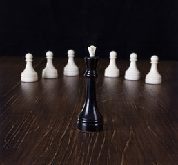 The Chess black queen in focus with white pawns.