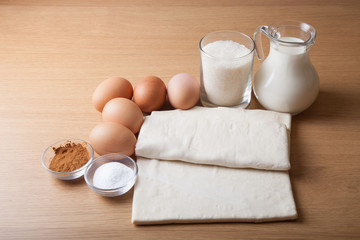 Milk, sugar, cocoa, puff dough, eggs and salt on a wooden board.