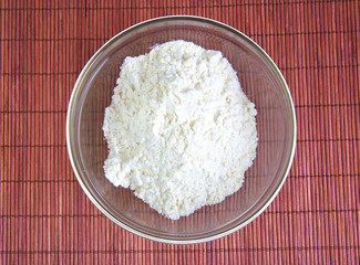 Flour in a glass bowl on wooden background.
