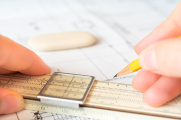 Hand holds the pencil and a slide rule to create a drawing. Angl